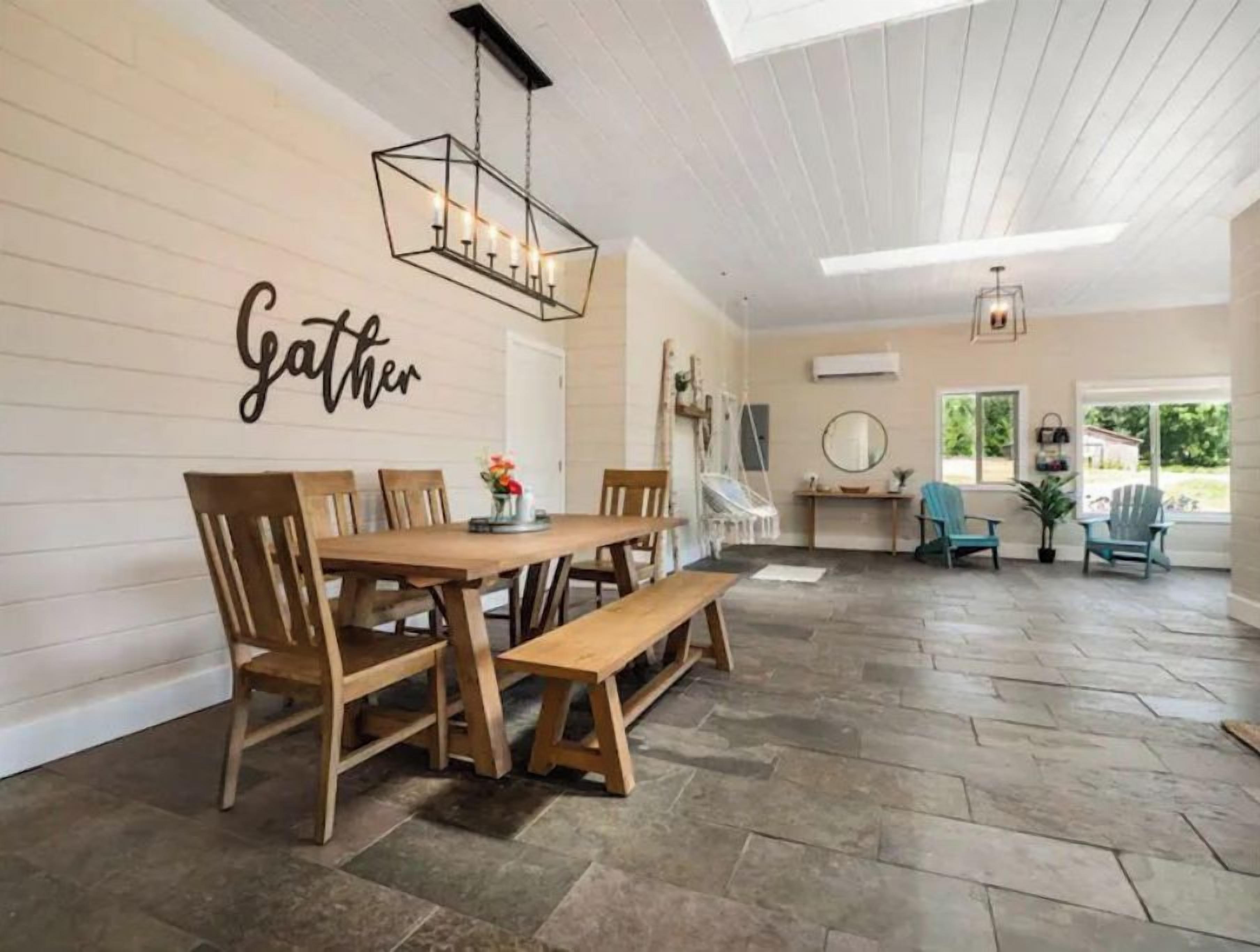 A dining area with a wooden table and chairs, a bench, and a wall-mounted sign that reads "Gather".