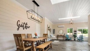 Ein Essbereich mit einem Holztisch und Stühlen, einer Bank und einem an der Wand befestigten Schild mit der Aufschrift 'Gather'.