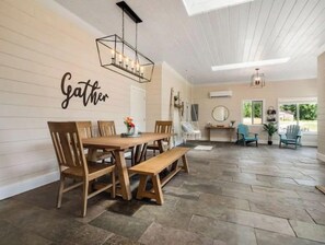 A dining area with a wooden table and chairs, a bench, and a wall-mounted sign that reads "Gather". - Charming 2BR Farmhouse Amazing View of Mt. Rainier - Family Friendly + Game Barn (Mineral)