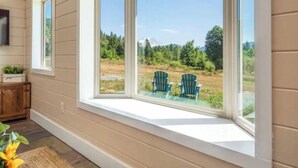 Ein Zimmer mit großem Erkerfenster mit Blick auf eine grüne Wiese und zwei Adirondack-Stühlen.