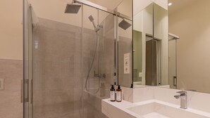 Un baño moderno con ducha de vidrio, un espejo grande y una encimera de mármol blanco.