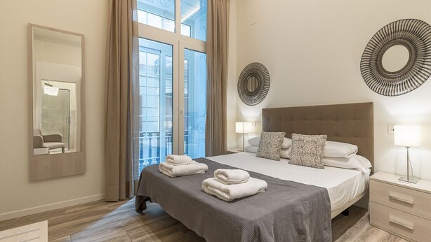 Habitación de hotel moderna con una cama grande, un espejo, una ventana con cortinas y vistas al exterior.