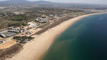 Vista aérea de una zona costera con una extensa playa de arena, un complejo edilicio con varias construcciones, y una clara vista del océano.