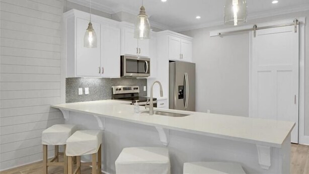 Una cocina moderna con armarios blancos, electrodomésticos de acero inoxidable e iluminación colgante.