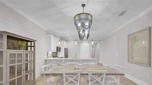 Un comedor espacioso con una gran mesa de madera, sillas blancas y una lámpara decorativa.