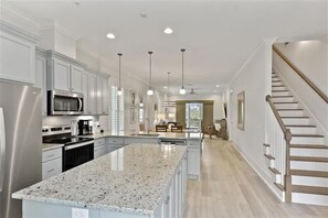 A spacious kitchen with granite countertops, stainless steel appliances, and pendant lighting. - Escape to The Moorings #42 (Jekyll Island)