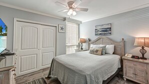 Quarto com cama, abajures, ventoinha no teto, mesa de cabeceira, relógio e janela com persianas.