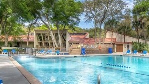 Uma piscina com cadeiras de descanso azuis, cercada por árvores e um edifício com telhado vermelho.
