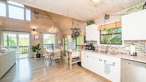 A spacious kitchen with wooden cabinets, a dining area with a table and chairs, and a large window overlooking greenery. - Canopy Ridge Retreat Cabin, couples oasis. Nature weddings (Sevierville)