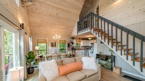 A spacious living area with a high ceiling, wooden walls, a staircase, and a dining area with a view of greenery. - Canopy Ridge Retreat Cabin, couples oasis. Nature weddings (Sevierville)