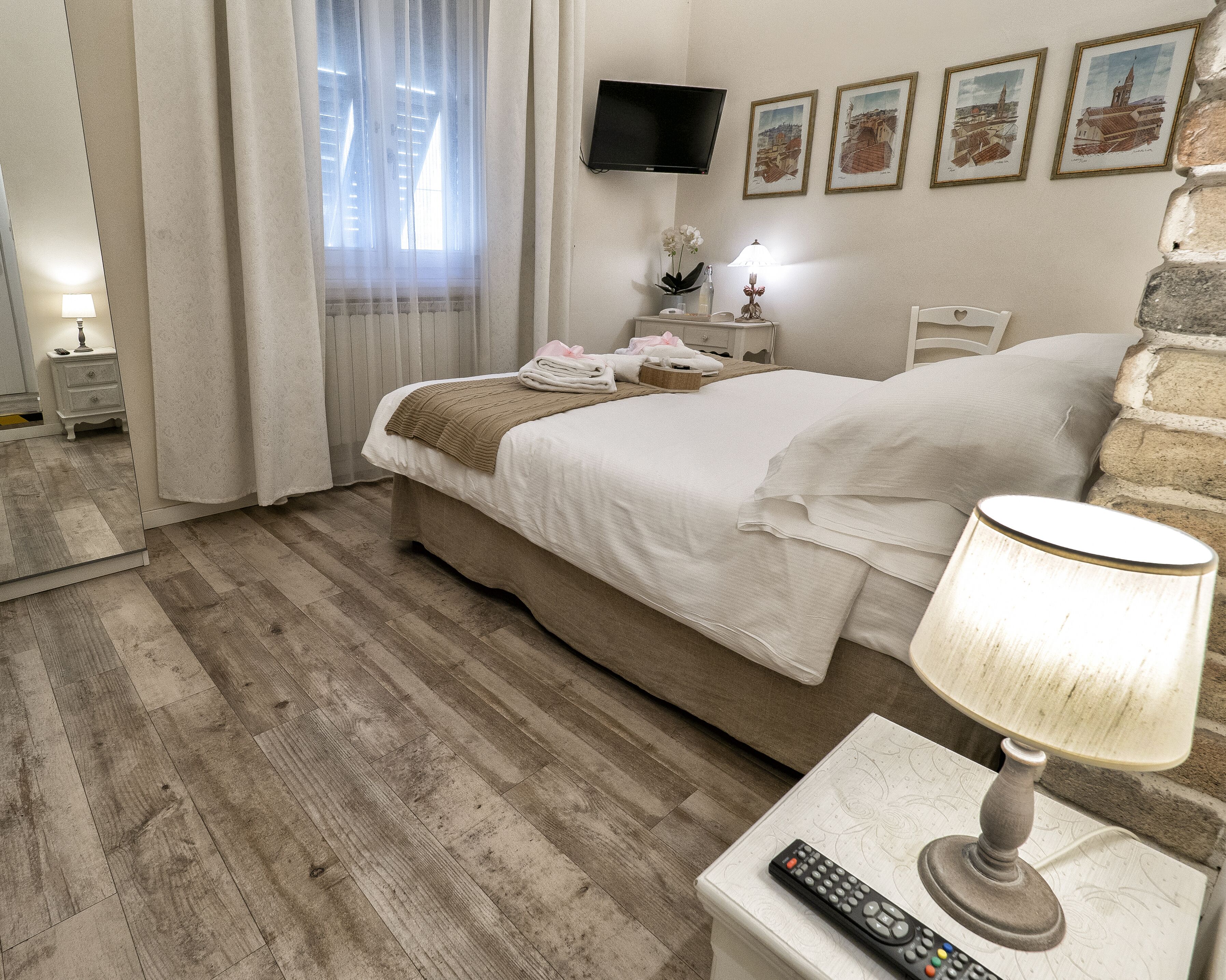 A hotel room with a bed, a nightstand, a lamp, a remote control, and framed pictures on the wall.