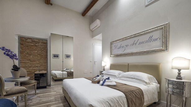A hotel room with a large bed, a desk with a chair, a small table with a lamp, and a stone accent wall. - BandBFirenze 8Cittadella8 (Florence)