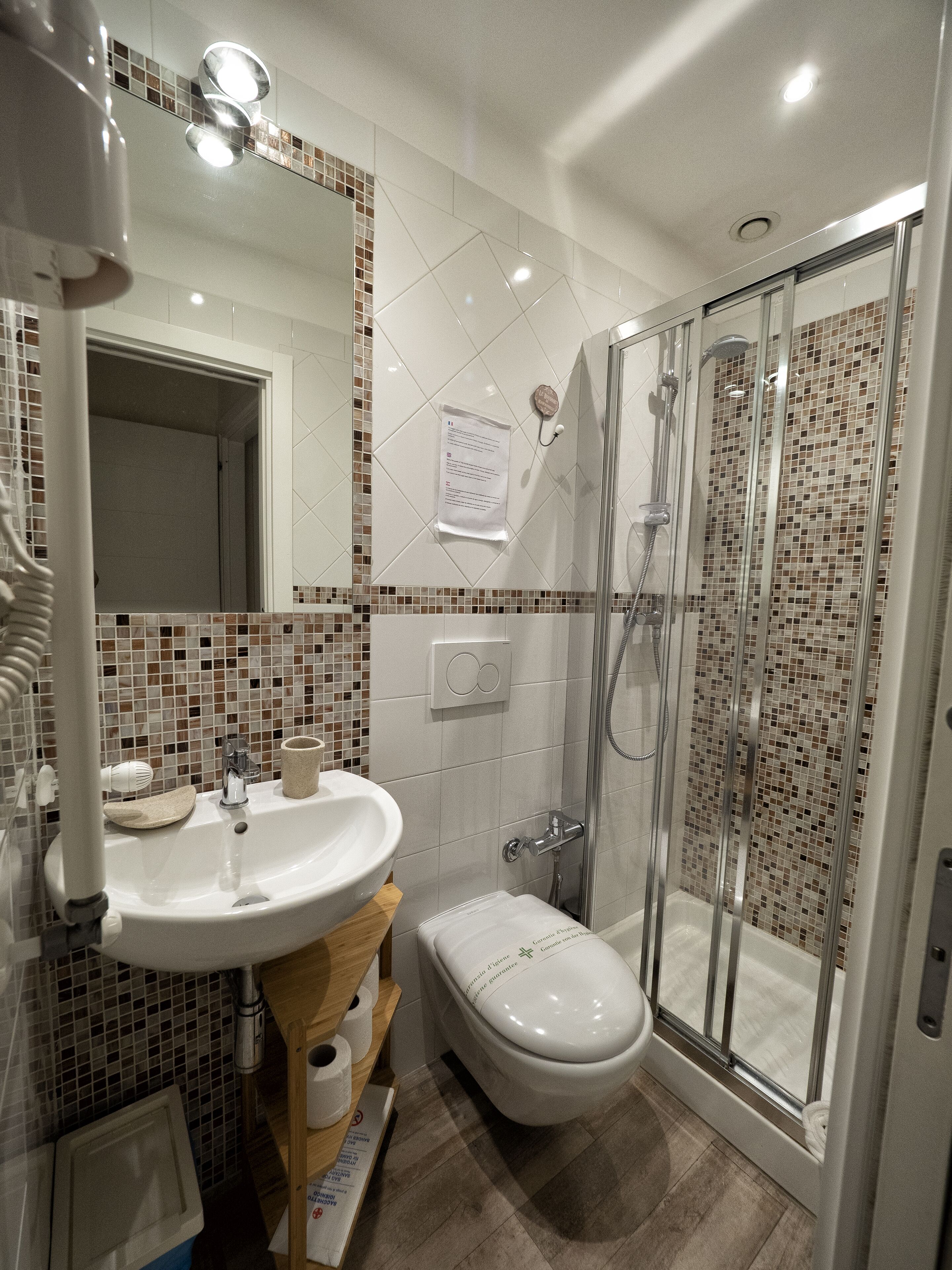 Et moderne badeværelse med en glasafskærmet brusekabine, et hvidt håndvaskarrangement og et toilet.