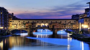 A historic bridge over a calm river at twilight, surrounded by buildings with illuminated windows. - BandBFirenze 8Cittadella8 (Florence)