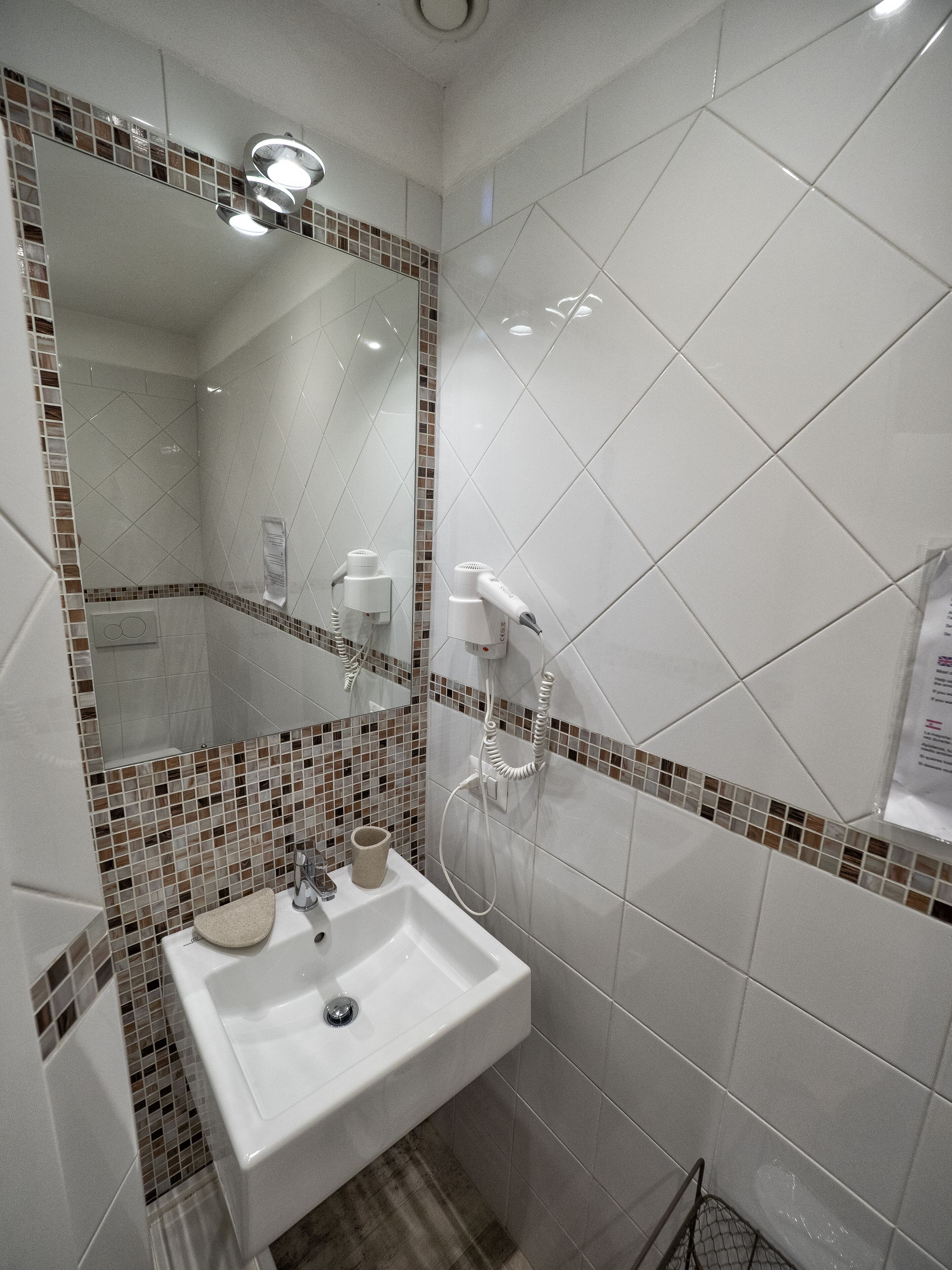 Un baño con un lavamanos blanco, un espejo y un secador de pelo montado en la pared.
