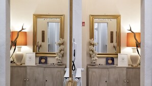 A mirrored hallway with a wooden floor, a beige cabinet with a white vase and a framed certificate, and a lamp with a decorative branch. - BandBFirenze 8Cittadella8 (Florence)