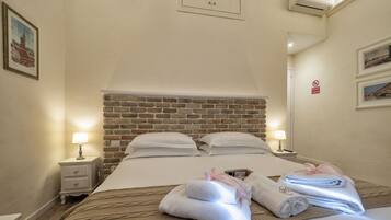 Ein Hotelzimmer mit Ziegelkopfteil, zwei weiße Betten mit Kissen, einem Nachttisch mit Lampe und einem Handtuchhalter mit Handtüchern.