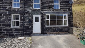 A stone house with a large window, a door, and a chimney. - Yr Hen Siop (Betws-Y-Coed)