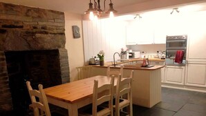 A cozy kitchen with a stone fireplace, wooden dining table, and white cabinets. - Yr Hen Siop (Betws-Y-Coed)