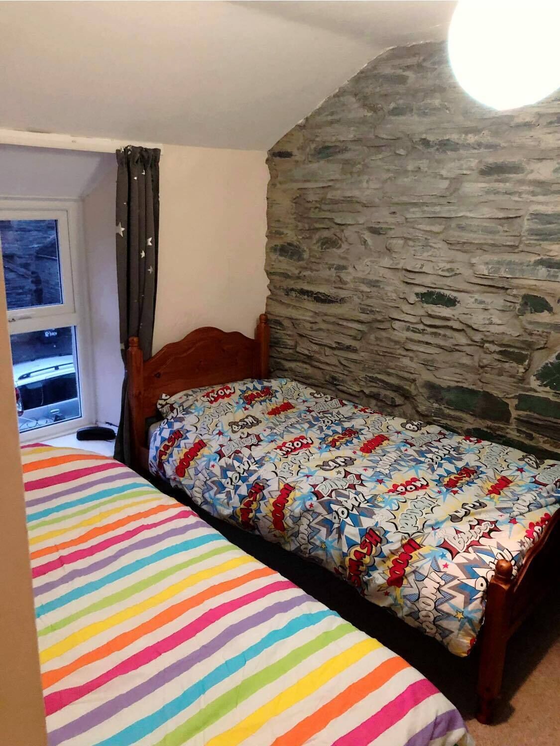 A bedroom with a single bed, a window with curtains, and a stone wall.