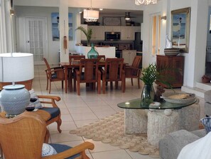 A spacious living room with a dining area, a kitchen in the background, and a view of the sea through a large window.