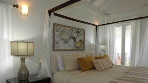 A bedroom with a four-poster bed, a nightstand with a lamp, a painting above the bed, and a view of the outdoors through the window. - "Atlantique" is a seaside space to be remembered! (Lowlands)