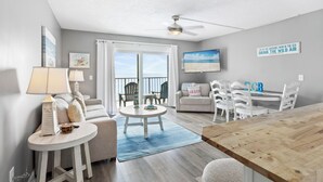 A modern living room with a wooden dining table, a sofa, and a ceiling fan. - Beachside Escape: Pool, Balcony, Free Chairs & More (Panama City Beach)