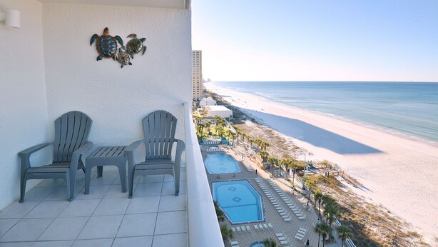 A balcony with two Adirondack chairs, a small pool, and a view of the beach and ocean. - Beachside Escape: Pool, Balcony, Free Chairs & More (Panama City Beach)