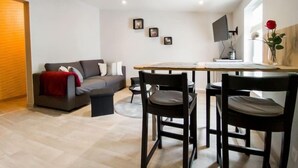 Un salon moderne avec un canapé gris, un plaid rouge et un coin repas comprenant une table et des chaises en bois.