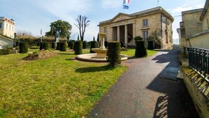 Un bâtiment de style classique, doté d’une fontaine centrale, entouré de haies soigneusement taillées et d’un chemin pavé.