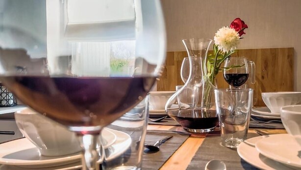 Une table à manger dressée avec des assiettes, des verres et des couverts, un verre à vin étant placé bien en évidence au premier plan.