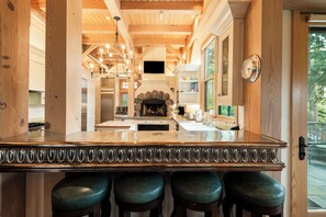 A kitchen with a central island, wooden beams, a stone fireplace, and a large window.