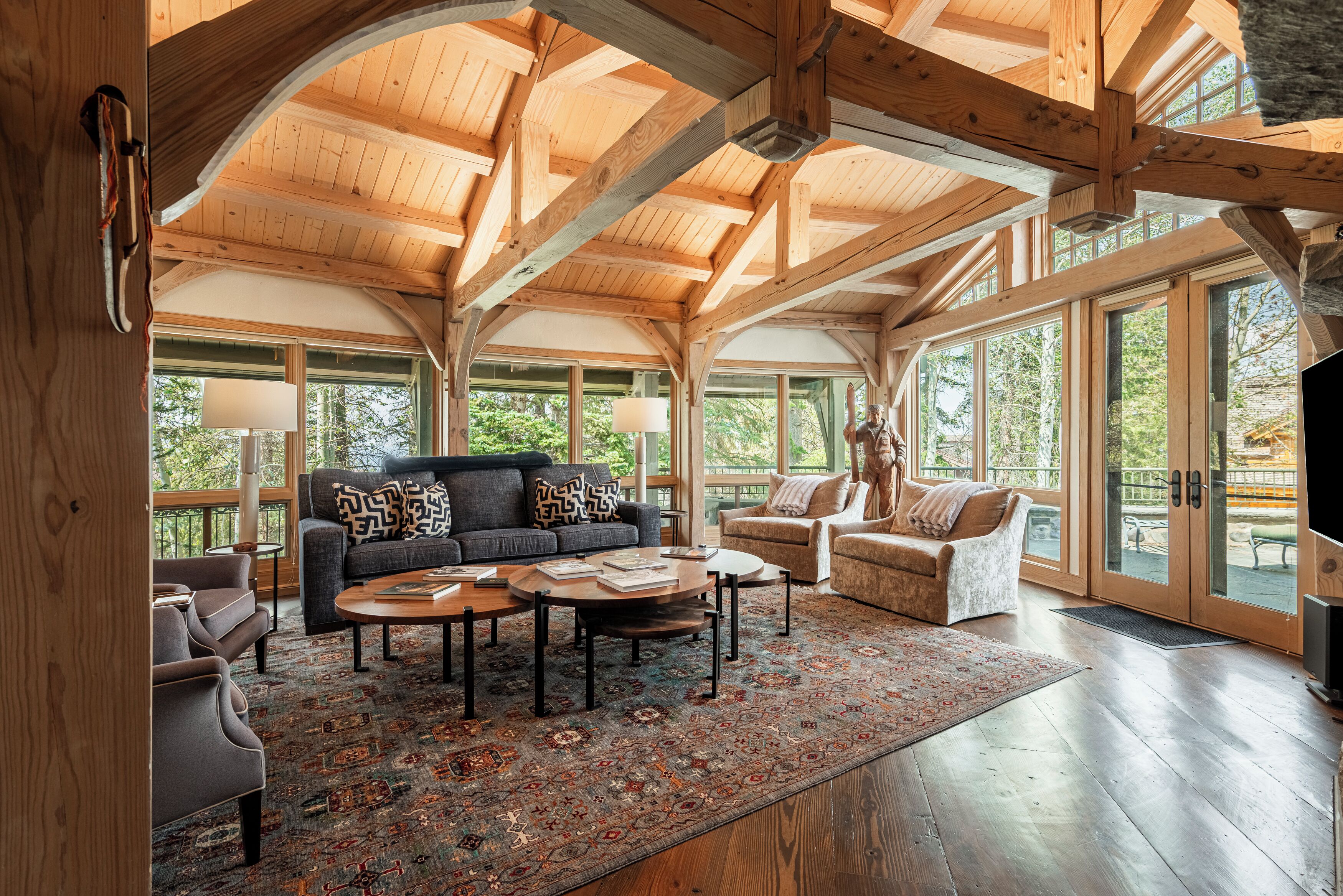 A spacious living room with a high wooden ceiling, large windows, and a cozy seating area with a sofa and armchairs.
