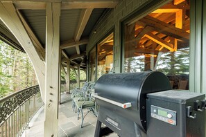 Een overdekt terras met een barbecue, stoelen en uitzicht op bomen.