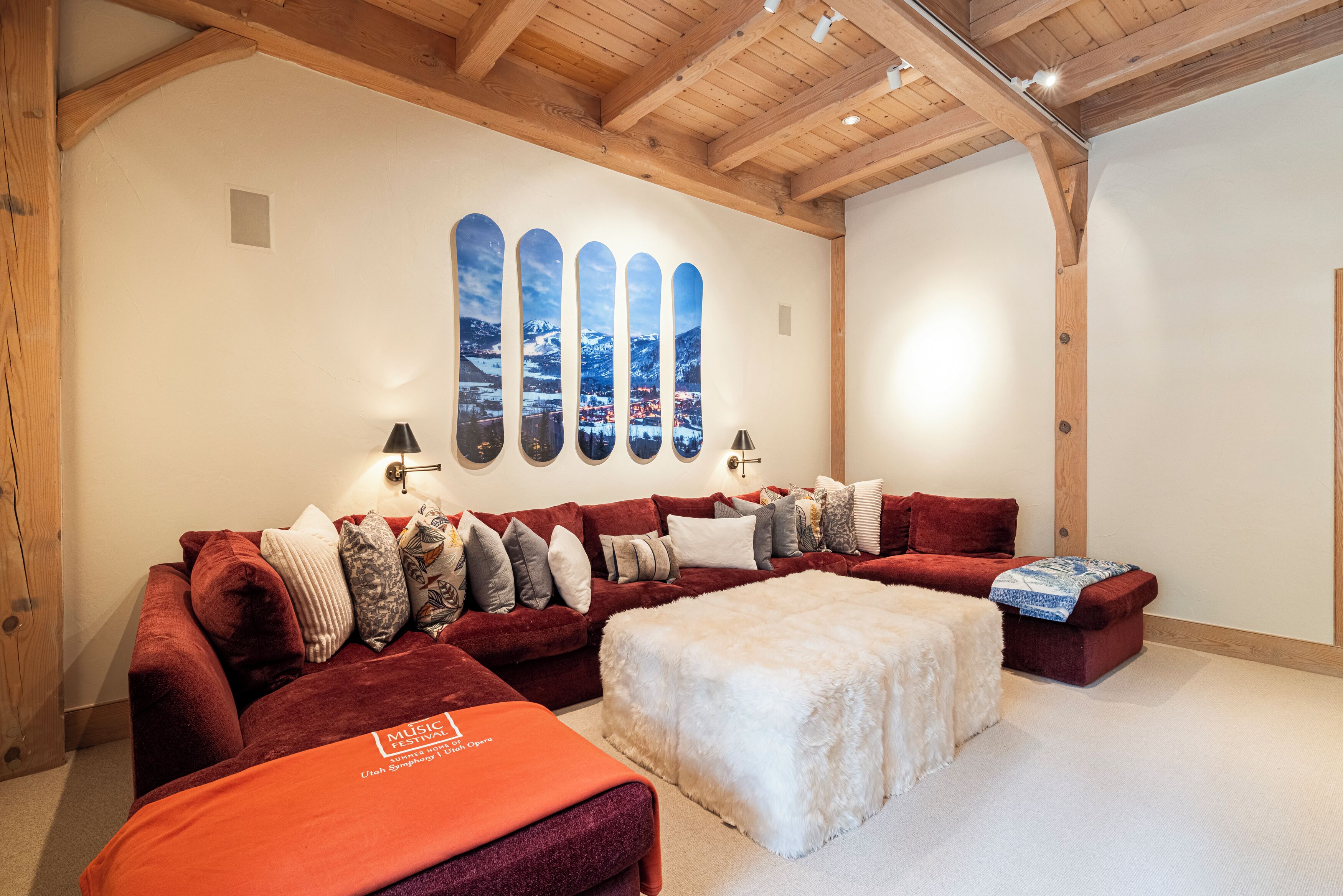 A cozy room with a red sofa, a white ottoman, and a wall with a scenic artwork.