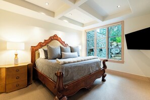 A bedroom with a wooden bed, a nightstand, a lamp, and a large window with a view of rocks and greenery.