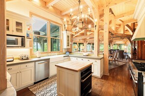 A modern kitchen with wooden beams, a large island, and a view of the outdoors.