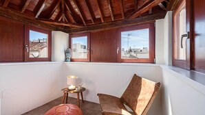 A cozy balcony with wooden beams, a cushioned chair, a small table with a lamp, and a view of the cityscape through wooden-framed windows. - Zabalza- Holiday rental in Malaga (Málaga)