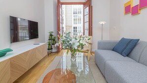 A modern living room with a flat-screen TV, a grey sofa, a coffee table, and a view of a building through an open door. - Zabalza- Holiday rental in Malaga (Málaga)