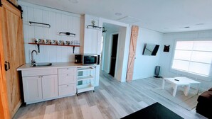 A modern kitchen with white cabinetry, a microwave, and a sink. There is a wooden door and a window with blinds. - **Minimalist Mtn Living- Pets Welcome (30+ Days)** (Fairplay)