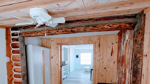 A hallway with wooden walls, a ceiling fan, a brick wall, and a door leading to a kitchen area. - **Minimalist Mtn Living- Pets Welcome (30+ Days)** (Fairplay)