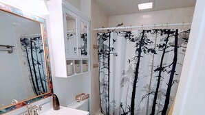 A bathroom with a white sink, wooden vanity, a toilet, and a shower curtain with a forest pattern. - **Minimalist Mtn Living- Pets Welcome (30+ Days)** (Fairplay)