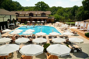A swimming pool surrounded by sun loungers and umbrellas, with a building in the background.