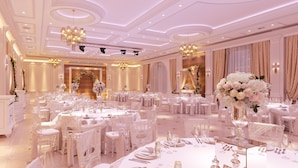 Un amplio salón de banquetes con mesas redondas, sillas blancas y elegantes candelabros.