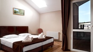 A hotel room with a bed, a radiator, a window with curtains, and a painting on the wall.