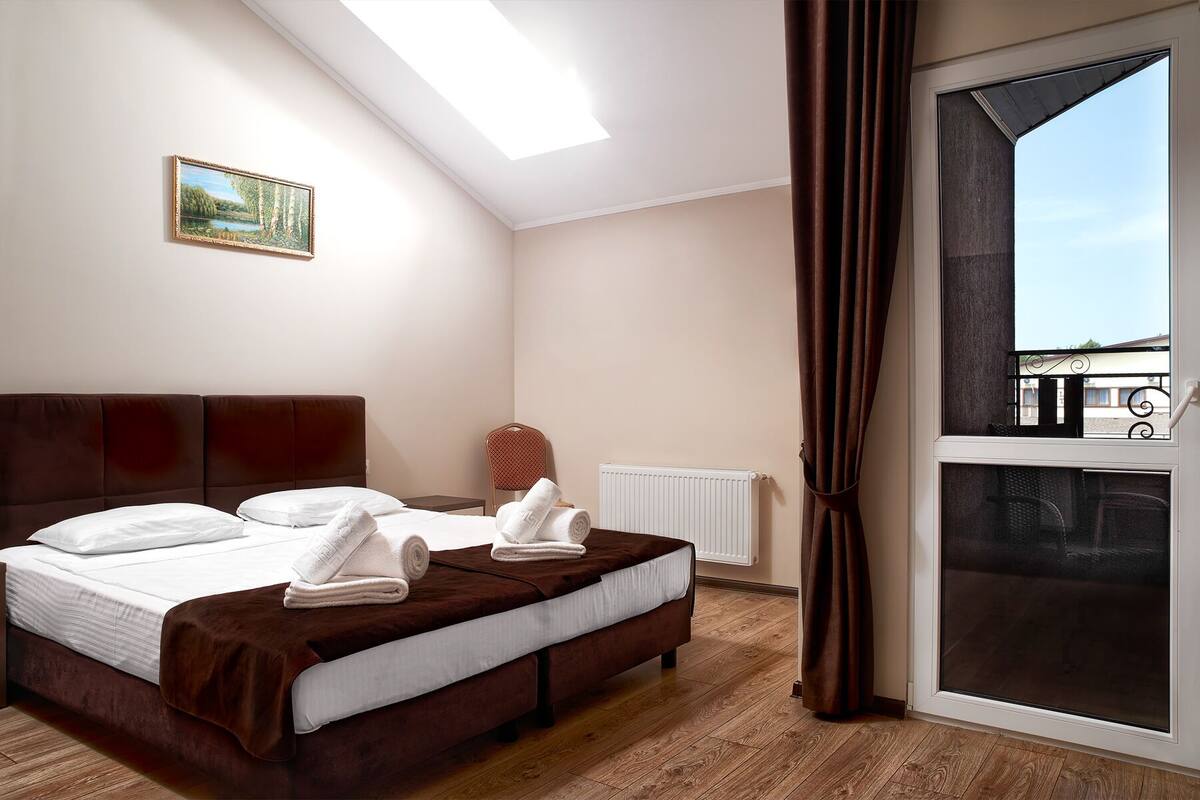 Quarto de hotel com uma cama grande, um radiador, uma janela com cortinas e um quadro na parede.