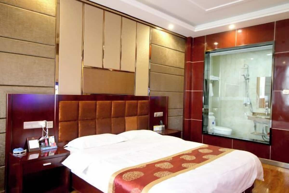 Habitación de hotel con una cama grande, una mesita de noche, ducha con cerramiento de vidrio y cabecero de madera.