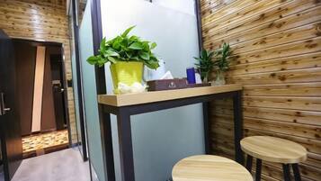 Una habitación pequeña con un muro de madera, una mesa con dos taburetes y una planta en maceta sobre la mesa.