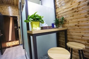 A small room with a wooden wall, a table with two stools, and a potted plant on the table. - Feitian Hotel (Jingyuan)