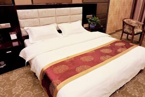 A neatly made bed with a white and red bedspread, a wooden nightstand with a lamp, and a chair with a floral pattern. - Feitian Hotel (Jingyuan)